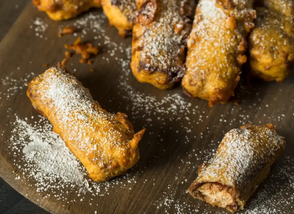 several deep fried mars bars on a chopping board covered in icing sugar