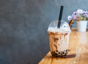 A creamy bubble tea with tapioca pearls on a wooden bench with a straw