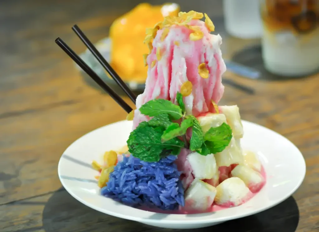 A shaved ice dessert piled high with colourful toppings and a set of chopsticks poking out of the side