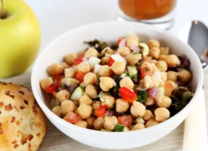 a bowl of chickpea salad with bread and an apple to one side