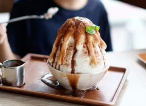 a bowl of south korean patbingsu topped with condensed milk and a mint leaf