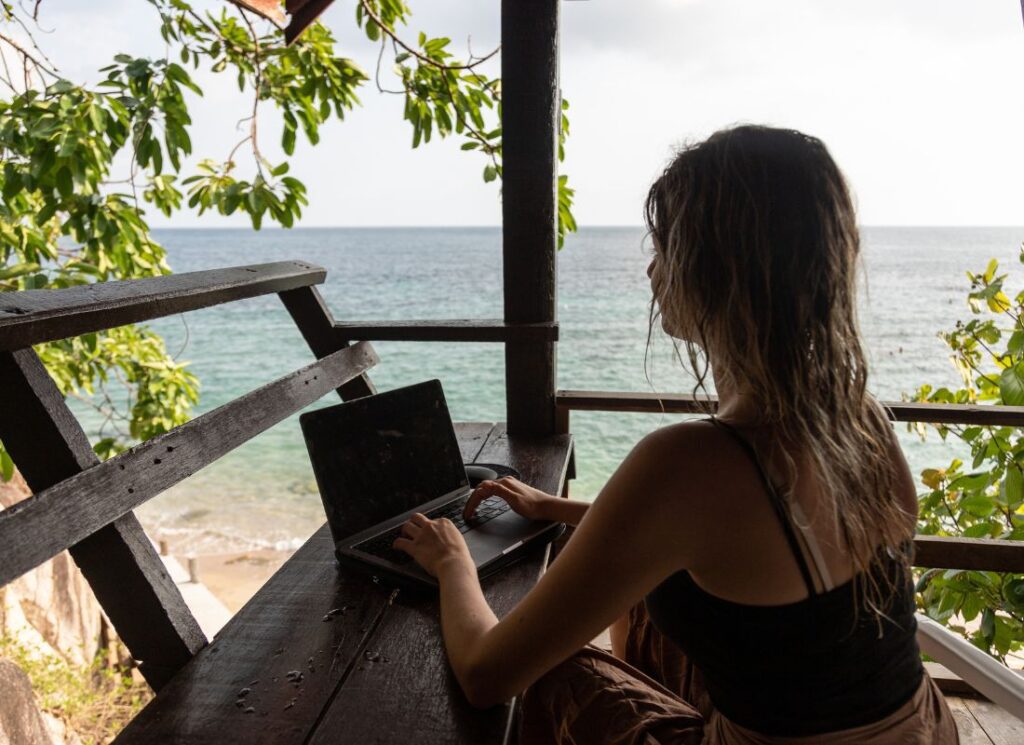 A digital nomad planning her packing list by the beach, facing the sea